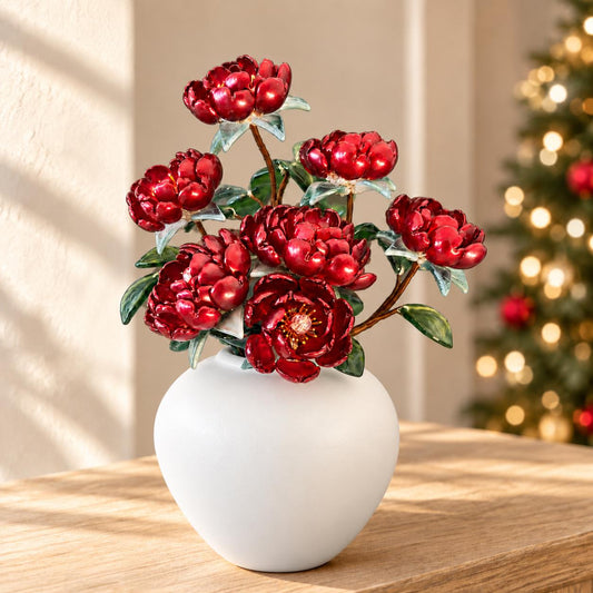 Red glass peony arrangement in white round vase beside a Christmas tree